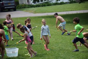 campers running through the grass in bathing suits squirting each other with water.