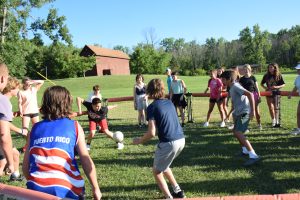 group of campers playing gaga in the grass while other campers stand around the outside of the gaga pit watching.
