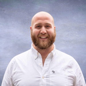 Taylor Headshot of a bald man with a brown bear and a white button down shirt