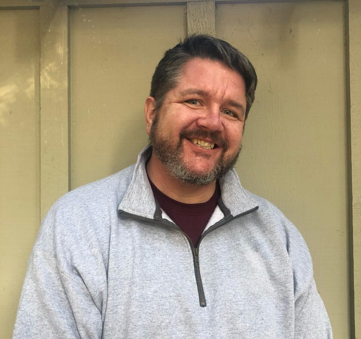 Headshot of a bald man with a brown bear and a white button down shirt